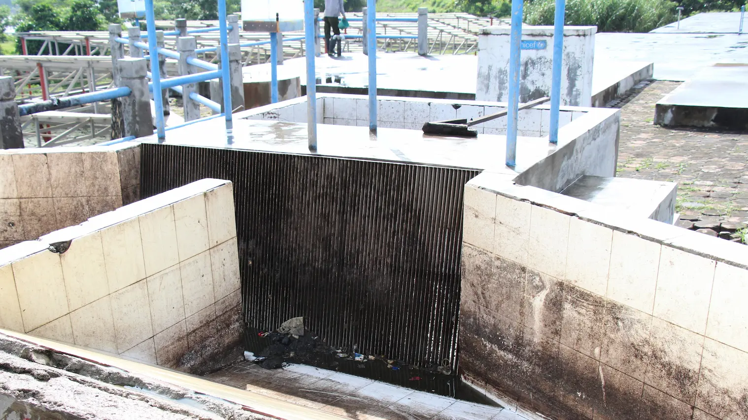 浄化槽汚泥処理施設のスクリーン部を示す写真。コンクリート製の槽の中に縦方向の金属棒が並んだスクリーンが設置されており、水中のごみや汚泥がスクリーン下部に引っかかっている。背景には配管や手すり、施設の構造物が見える。